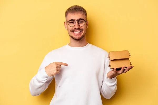 Young Caucasian Man Holding Burger Isolated Yellow Background Person Pointing — ストック写真