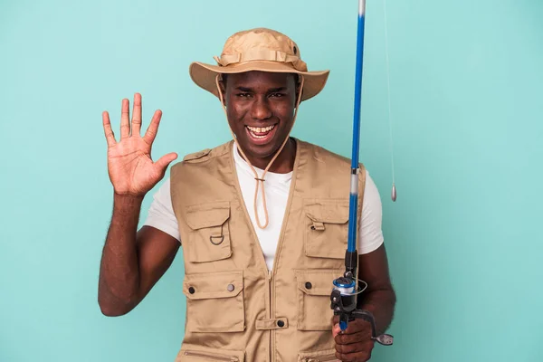 若いアフリカ系アメリカ人の漁師を保持ロッド青の背景に孤立笑顔陽気に数字5とともに指 — ストック写真