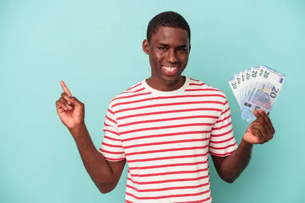 Mladý Afroameričan Drží Bankovky Izolované Modrém Pozadí Usmívá Ukazuje Stranou — Stock fotografie