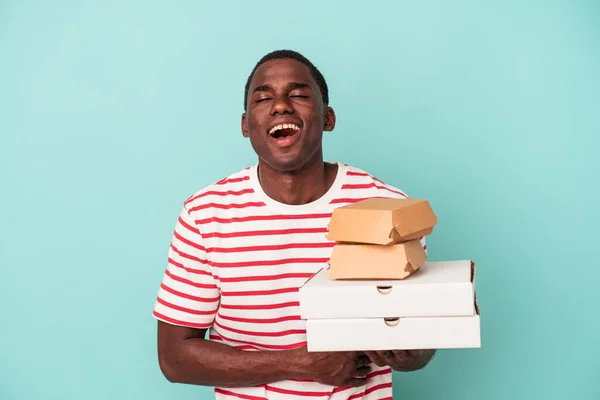 Mladý Afroameričan Drží Pizzy Hamburgery Izolované Modrém Pozadí Smíchem Baví — Stock fotografie