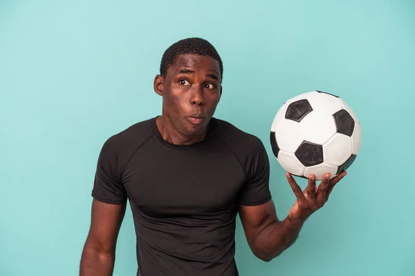 Młody Afroamerykanin Gra Piłkę Nożną Odizolowany Niebieskim Tle Wzrusza Ramionami — Zdjęcie stockowe