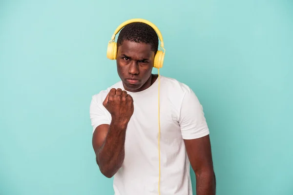 若いアフリカ系アメリカ人の男性は カメラに拳を示す青い背景に隔離された音楽を聞いて 積極的な顔の表情 — ストック写真