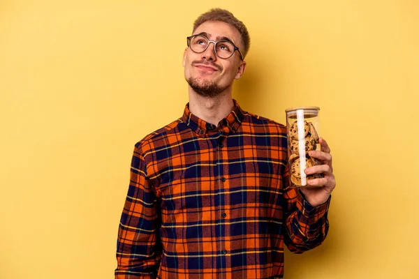 Young Caucasian Man Holding Cookies Jar Isolated Yellow Background Dreaming — Stock fotografie