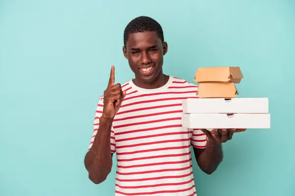 Joven Afroamericano Sosteniendo Pizzas Hamburguesas Aisladas Sobre Fondo Azul Mostrando —  Fotos de Stock