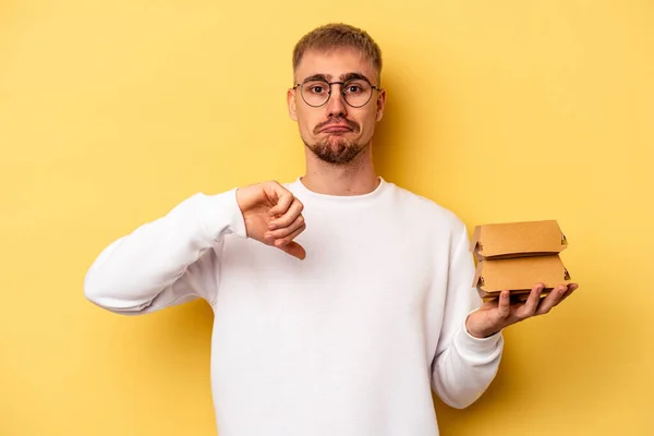 Young Caucasian Man Holding Burger Isolated Yellow Background Showing Dislike — ストック写真