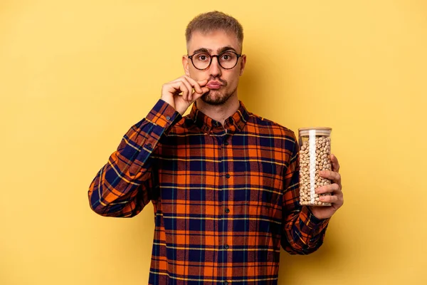 Young Caucasian Man Holding Chickpeas Isolated Yellow Background Fingers Lips — Zdjęcie stockowe