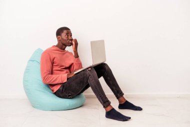 Genç Afrikalı Amerikalı bir adam laptopunu kullanıyor. Beyaz arka planda izole edilmiş, tırnaklarını yiyor. Gergin ve endişeli..