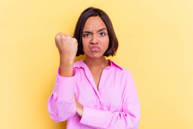Sarı arka planda izole edilmiş genç bir ırk kadını kameraya yumruk gösteriyor, agresif bir yüz ifadesi..