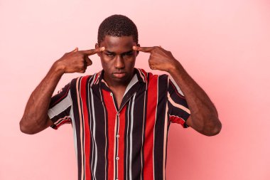 Pembe arka planda izole edilmiş genç Afrikalı Amerikalı bir adam bir göreve odaklanmış, işaret parmaklarını işaret ediyor..
