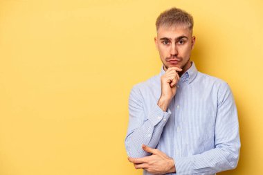 Sarı arka planda izole edilmiş genç beyaz adam şüpheli ve şüpheci bir ifadeyle yana bakıyor..