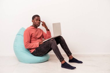 Beyaz arka planda izole edilmiş dizüstü bilgisayar kullanan genç Afrikalı Amerikalı adam işaret parmağıyla yaptığı hayal kırıklığı jestini gösteriyor..