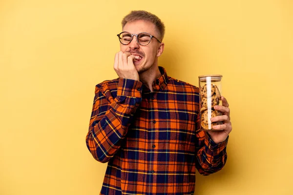 Young Caucasian Man Holding Cookies Jar Isolated Yellow Background Biting — Photo
