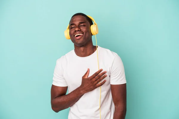 若いアフリカ系アメリカ人の男は青い背景に隔離された音楽を聞いて笑う大声で手を胸に保つ — ストック写真
