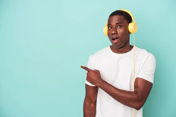 若いアフリカ系アメリカ人の男性が音楽を聞いている側を指している青の背景に孤立 — ストック写真