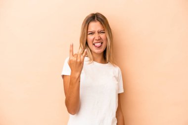 Beyaz tenli genç bir kadın bej arka planda izole edilmiş. Parmaklarıyla taş hareketi gösteriyor.