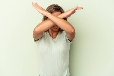 Genç beyaz kadın yeşil arka planda izole edilmiş iki kolu çapraz tutuyor, inkar kavramı.