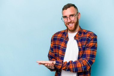 Mavi arka planda izole edilmiş genç beyaz bir adam palmiyesinde bir kopya alanı tutuyor..