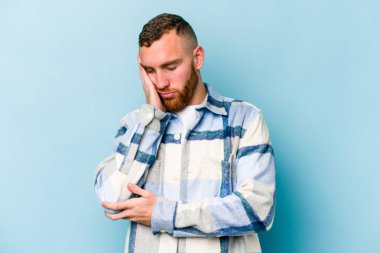 Mavi arka planda izole edilmiş, sıkılmış, yorgun ve dinlenmeye ihtiyacı olan genç beyaz bir adam..