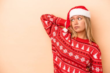 Young caucasian woman celebrating Christmas isolated on beige background touching back of head, thinking and making a choice.