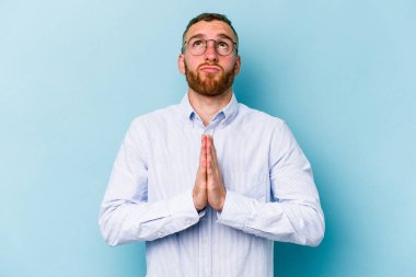 Mavi arka planda izole edilmiş genç beyaz bir adam el ele tutuşup, ağzının kenarında dua ediyor, kendinden emin..