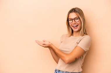 Beyaz tenli genç bir kadın, bej arka planda izole edilmiş. Elinde palmiye ağacında bir kopya alanı var..