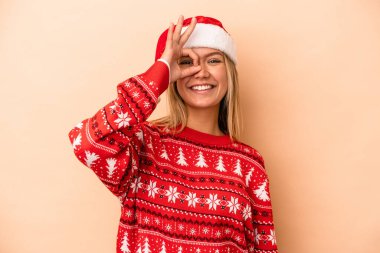 Young caucasian woman celebrating Christmas isolated on beige background excited keeping ok gesture on eye.