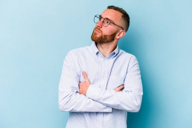 Kafkasyalı genç adam mavi arka planda izole edilmiş hedeflerine ve amaçlarına ulaşma hayali kuruyor.