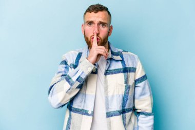 Mavi arka planda izole edilmiş genç beyaz bir adam ya sır saklıyor ya da sessizlik istiyor..