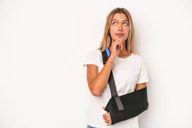 Young caucasian woman with broken hand isolated on white background looking sideways with doubtful and skeptical expression.