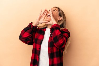 Beyaz tenli genç bir kadın bej arka planda izole edilmiş ve heyecanlı bir şekilde bağırıyor..