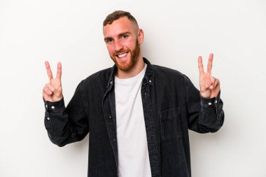 Beyaz arka planda izole edilmiş genç beyaz bir adam zafer işareti gösteriyor ve gülümsüyor..