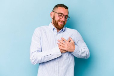 Mavi arka planda izole edilmiş beyaz bir genç, dost bir ifadeye sahip, avuçlarını göğsüne bastırıyor. Aşk konsepti.