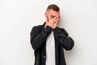 Beyaz arka planda izole edilmiş genç beyaz bir adam kameraya parmaklarıyla göz kırpıyor, yüzünü kapatmaktan utanıyor..