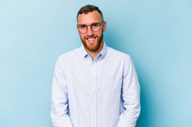 Kafkasyalı genç, mavi arka planda izole edilmiş. Kendine güvenen, kalçaları tutan biri..