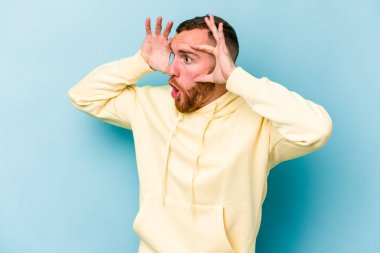 Mavi arka planda izole edilmiş genç beyaz adam bir başarı fırsatı bulmak için gözlerini açık tutuyor..