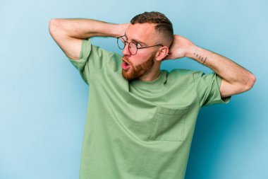 Genç beyaz adam mavi arka planda izole edilmiş bağırıyor, çok heyecanlı, tutkulu, bir şeyden memnun..