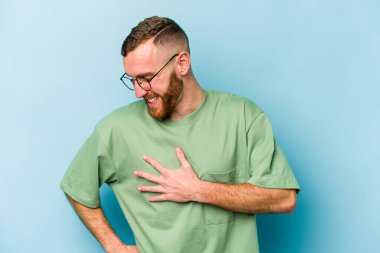 Kafkasyalı genç adam mavi arka planda izole olmuş gülüyor, elini yüreğine koyuyor, mutluluk kavramını koruyor..