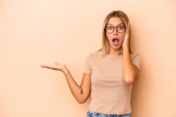 Mujer Joven Caucásica Aislada Sobre Fondo Beige Impresionada Sosteniendo Espacio — Foto de Stock