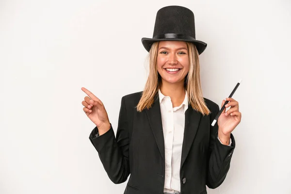 Young caucasian wizard woman holding wand isolated on white background smiling and pointing aside, showing something at blank space.