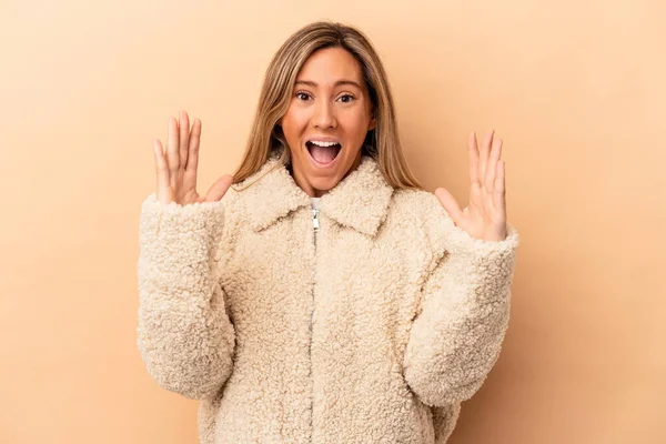 Beyaz tenli genç bir kadın bej arka planda izole edilmiş. Hoş bir sürprizle karşılaşıyor. Heyecanlı ve el kaldırıyor..