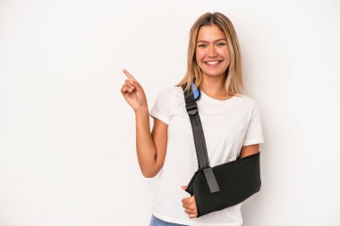 Young caucasian woman with broken hand isolated on white background smiling and pointing aside, showing something at blank space.
