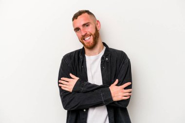 Beyaz arka planda kendini güvende hisseden, kararlılıkla kollarını kavuşturan beyaz tenli genç bir adam..