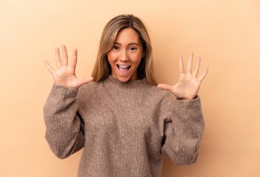 Beyaz tenli genç bir kadın bej arka planda izole edilmiş. Hoş bir sürprizle karşılaşıyor. Heyecanlı ve el kaldırıyor..