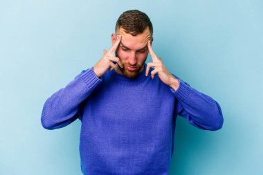Kafkasyalı genç bir adam mavi arka planda izole edilmiş, başı ağrıyor, yüzüne dokunuyor..