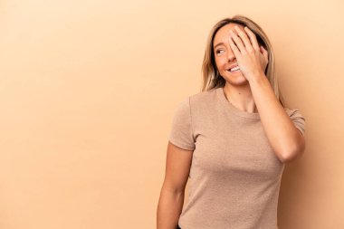 Beyaz tenli genç bir kadın bej arka planda izole edilmiş gülerek, kaygısızca, doğal duygularla gülüyor..