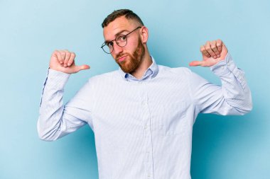 Mavi arka planda izole edilmiş genç beyaz adam gururlu ve kendinden emin hissediyor, örnek olarak.