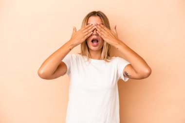 Beyazlı genç bir kadın bej arka planda izole edilmiş. Gözleri elleriyle kapamaktan korkuyor..