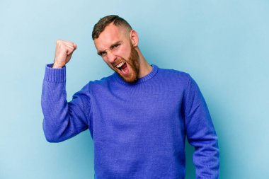 Kafkasyalı genç adam mavi arka planda izole edilmiş kaygısız ve heyecanlı tezahüratlar yapıyor. Zafer konsepti.