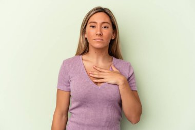 Genç beyaz kadın yeşil arka planda izole edilmiş yemin ediyor, elini göğsüne koyuyor..