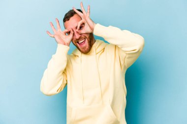 Mavi arka planda izole edilmiş genç beyaz adam gözlerinde sorun olmadığını gösteriyor.